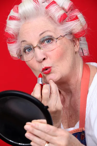 Grootmoeder met haar haren in rollen toe te passen lippenstift — Stockfoto