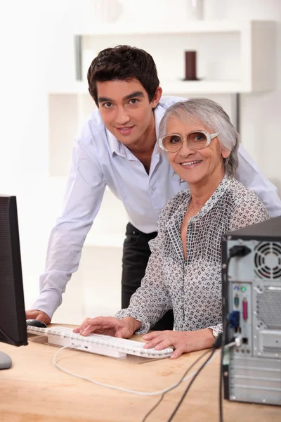 Enkel erklärt Großmutter die Bedienung eines Computers — Stockfoto
