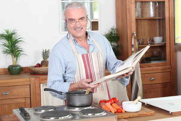 Muž připravuje jídlo s pomocí kuchařka — Stock fotografie