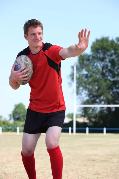 Rugby player holding the ball tight to his chest mid game — Stock Photo, Image
