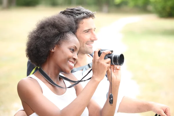 Couple sat at the beach holding camera — Stockfoto