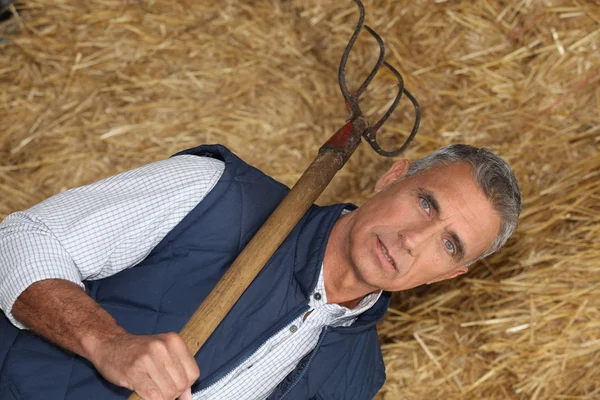 Maturo bello contadino posa con forchetta contro fieno sfondo — Foto Stock