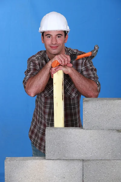 Constructeur avec marteau et bois à côté d'un mur de bloc — Photo