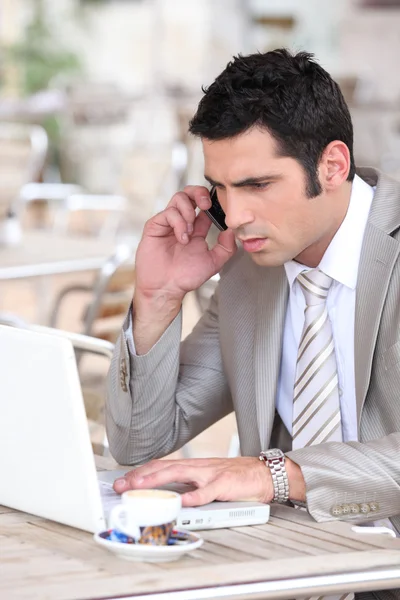 Businessman on phone working on laptop — Stockfoto