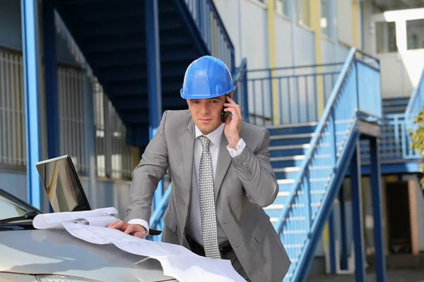 Architect on site with plans and cellphone — Stockfoto