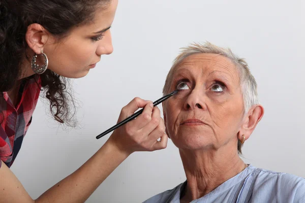 Woman applying makeup to an older lady — Stockfoto
