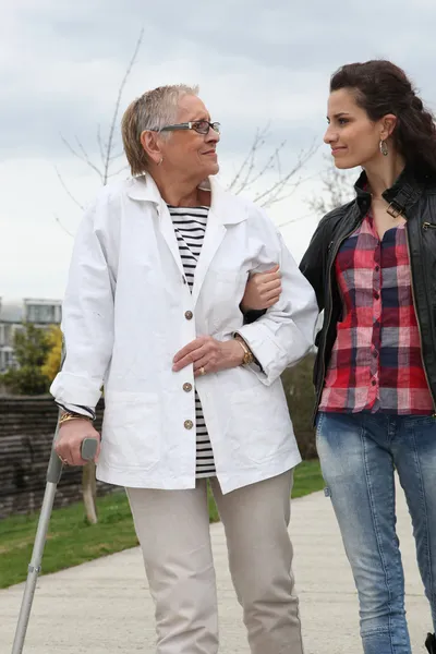 Jovem mulher ajudando a pessoa idosa a andar com uma muleta — Fotografia de Stock