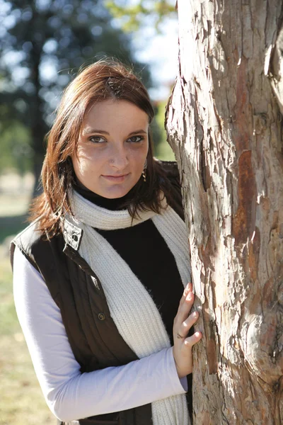 Jovem mulher em pé junto a uma árvore — Fotografia de Stock