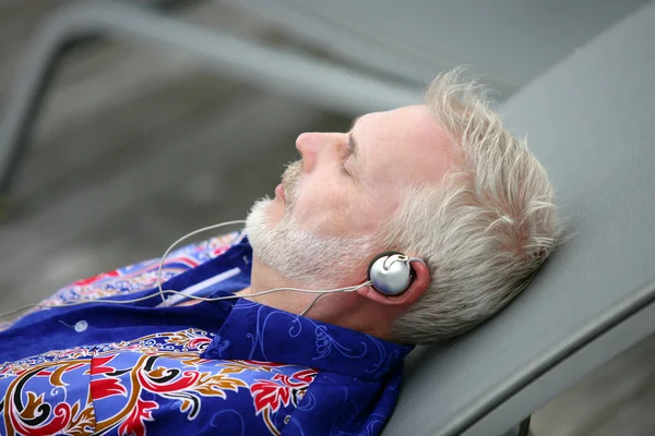 Man laying on deck chair listening to music — Stockfoto