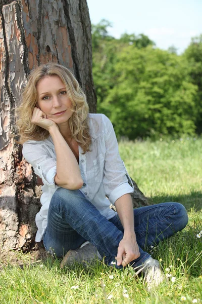 Woman sitting against tree — Stockfoto