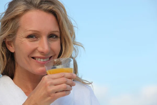 Closeup of a woman in a bathrobe drinking orange juice outdoors — Stock Photo, Image