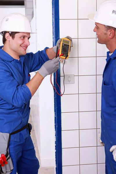 Two young plumbers larking about with a voltmeter — Stockfoto