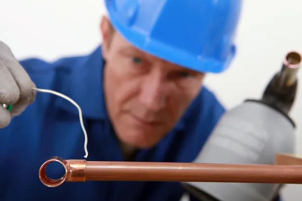 Skilled tradesman in blue jumpsuite is soldering a copper pipe — Stok fotoğraf