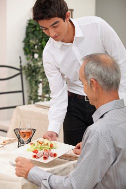 Young waiter serving ham salad clipart