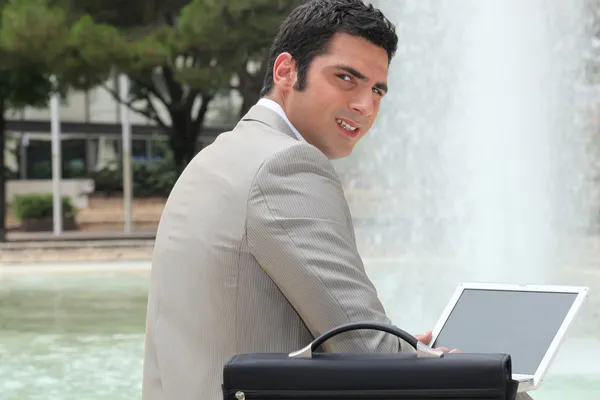 Uomo d'affari che utilizza un computer portatile all'aperto da una fontana — Foto Stock