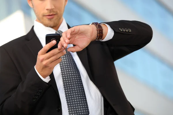 Joven ejecutivo comprobando su reloj contra un teléfono celular — Foto de Stock