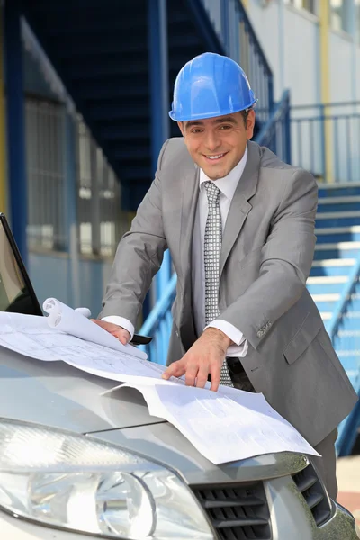 Architect looking at plans on a car bonnet — Stock Photo, Image