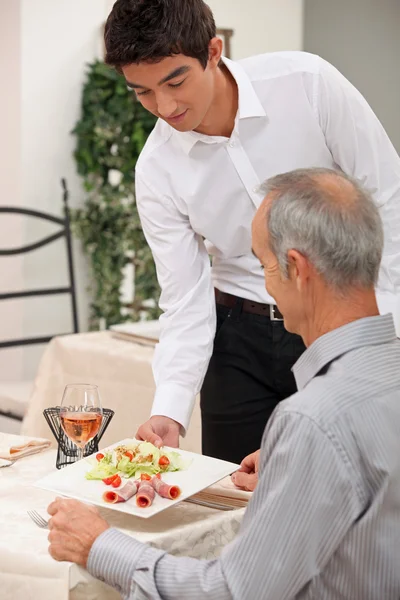 Ung servitör som serverar skinka sallad — Stockfoto