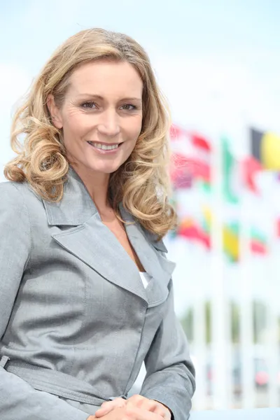Mujer sonriente ejecutiva frente a banderas del mundo —  Fotos de Stock