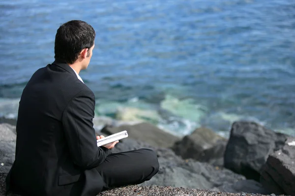 Бизнесмен сидел на скале у моря — стоковое фото