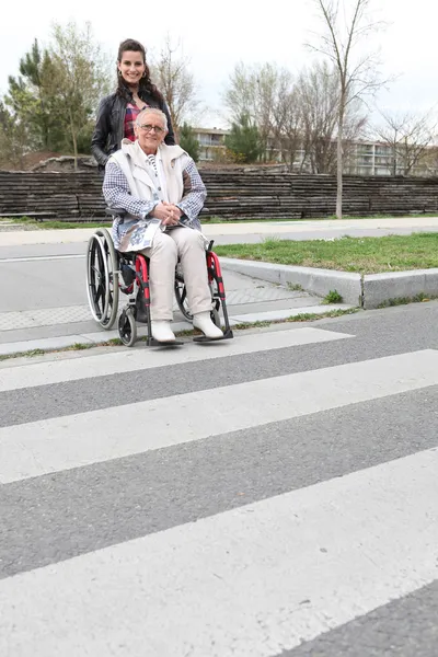 Mulher esperando em uma zebra cruzando com uma senhora idosa em uma cadeira de rodas — Fotografia de Stock