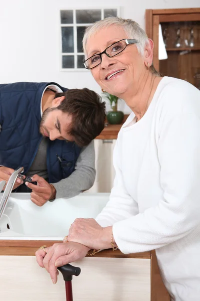 Разнорабочий чинит кухонный кран для пожилой женщины — стоковое фото