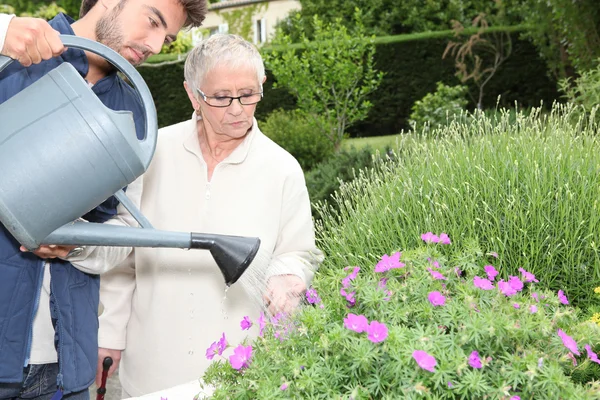 Ung man vattna växter med äldre kvinna — Stockfoto
