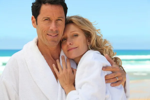 Casal de meia idade vestindo um roupão de banho perto do mar — Fotografia de Stock