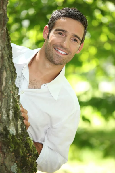 Zabawa w chowanego. człowiek w białej koszuli wpatrując się wokół drzewa. — Zdjęcie stockowe