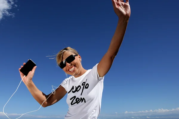Woman wearing sunglasses listening to music through digital player — Stock Photo, Image