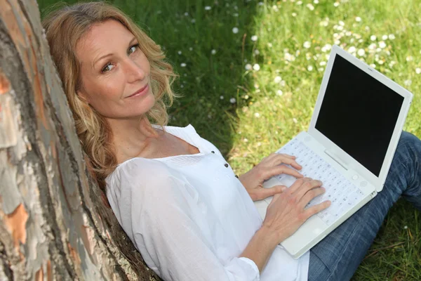 Kobieta pod drzewem przy pomocy pewien laptop z ekranem puste dla wiadomości — Zdjęcie stockowe