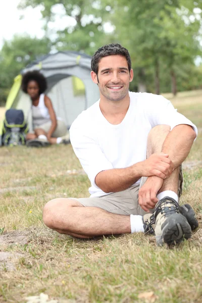 A man seated, behind him, a canvas tent and a woman — Stock Photo, Image