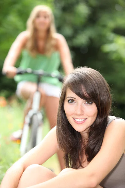 Junge Frau sitzt mit ihrem Freund auf einem Fahrrad im Hintergrund im Gras — Stockfoto