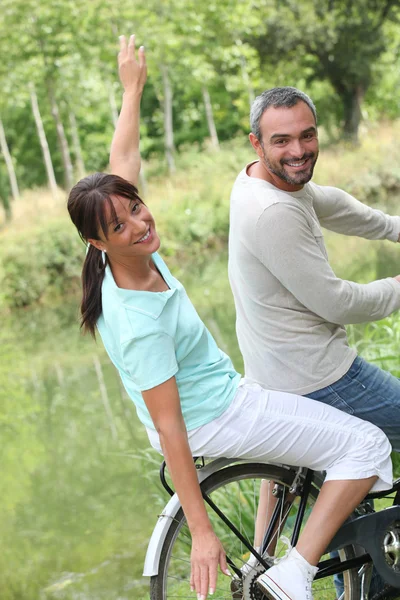 Um casal fazendo bicicleta no campo, a mulher está fazendo avião com seu ar — Fotografia de Stock