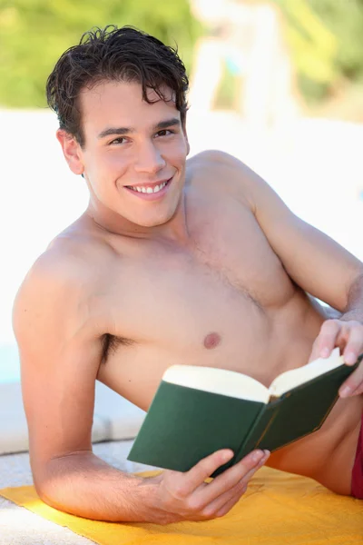 Чоловік покладений на пляжний рушник читання книги — стокове фото
