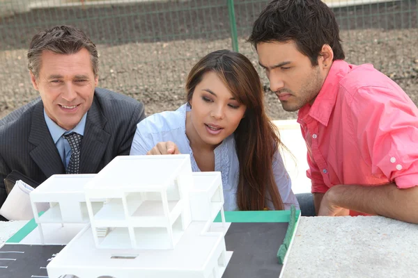 Agent and young couple with a model of a new development — Stock Photo, Image
