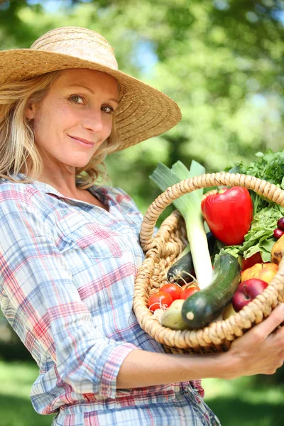 Mulher com um chapéu de palha segurando cesta de legumes . — Fotografia de Stock