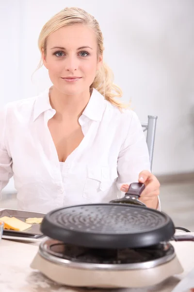 Mujer rubia frente a un calentador preparando queso derretido, patatas y col —  Fotos de Stock