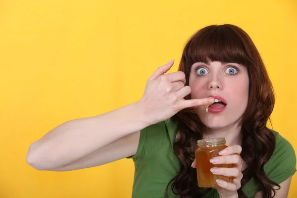 Frau taucht Finger in Honigglas — Stockfoto