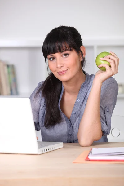 Женщина с яблоком сидит за ноутбуком — стоковое фото