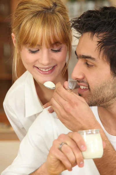 Man feeding a spoonful of yoghurt to his girlfriend — Stock Photo, Image