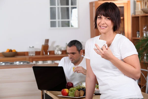Mujer bebiendo café mientras su marido mira su computadora portátil durante los desayunos —  Fotos de Stock