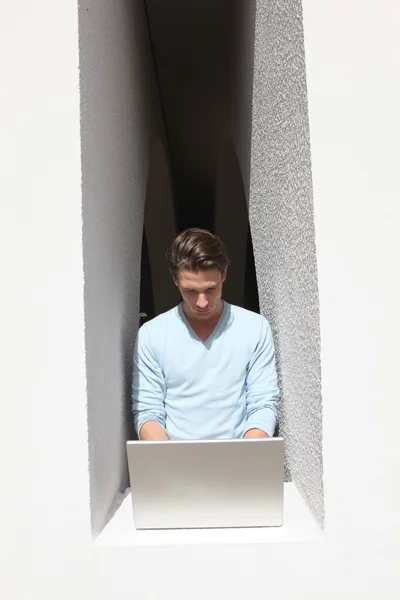 Homem usando o computador portátil pela borda da janela — Fotografia de Stock