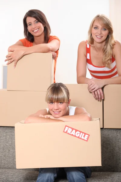 Tres mujeres jóvenes posando en una habitación llena de paquetes desempaquetados —  Fotos de Stock