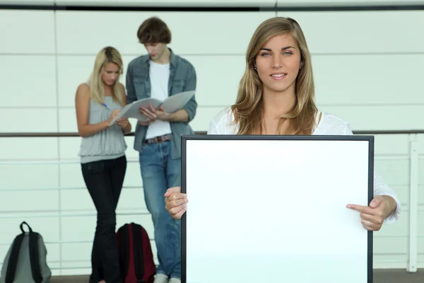 Young woman holding and pointing to a blank sign — Stock Photo, Image