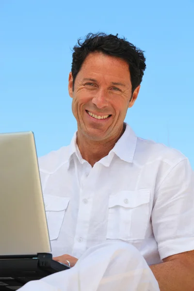 Uomo sorridente sul computer portatile nel cielo blu — Foto Stock