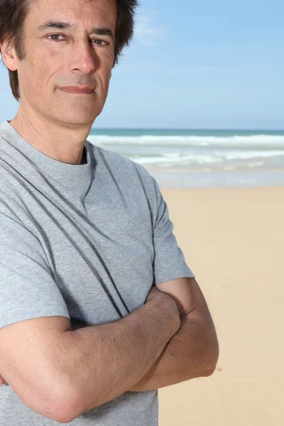 Человек, стоящий со скрещенными руками на песчаном пляже — стоковое фото