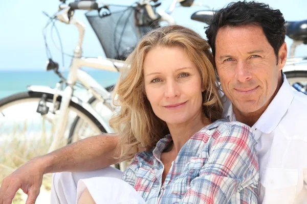 Счастливая пара, сидящая на пляже со своими велосипедами — стоковое фото