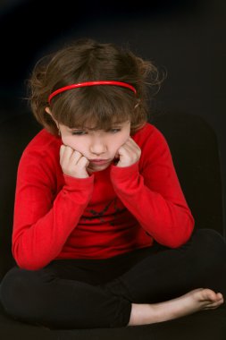 Little girl pouting with face resting on hands against black background clipart