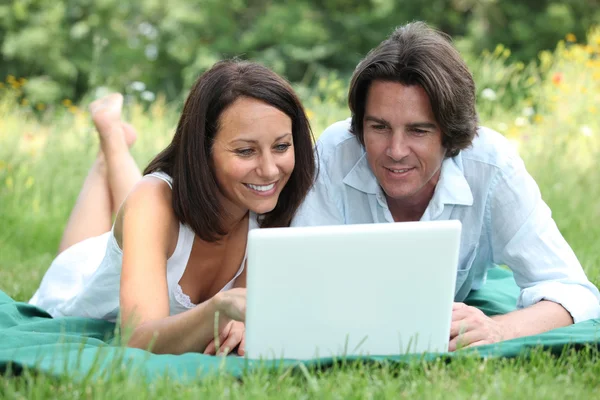 ラップトップ コンピューターの画面を見ながら草の上に横たわるカップル — ストック写真
